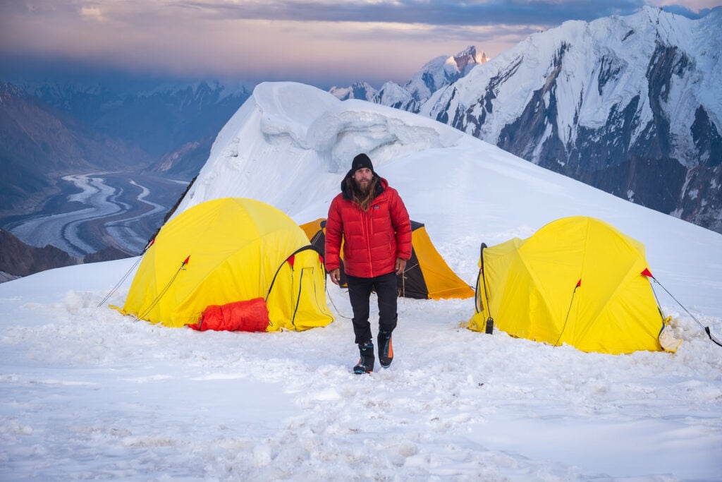 a man standing next to a couple of tents on top of a snow covered mountain