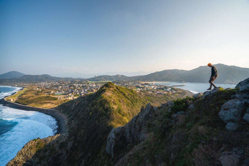 a man standing on top of a mountain next to the ocean.